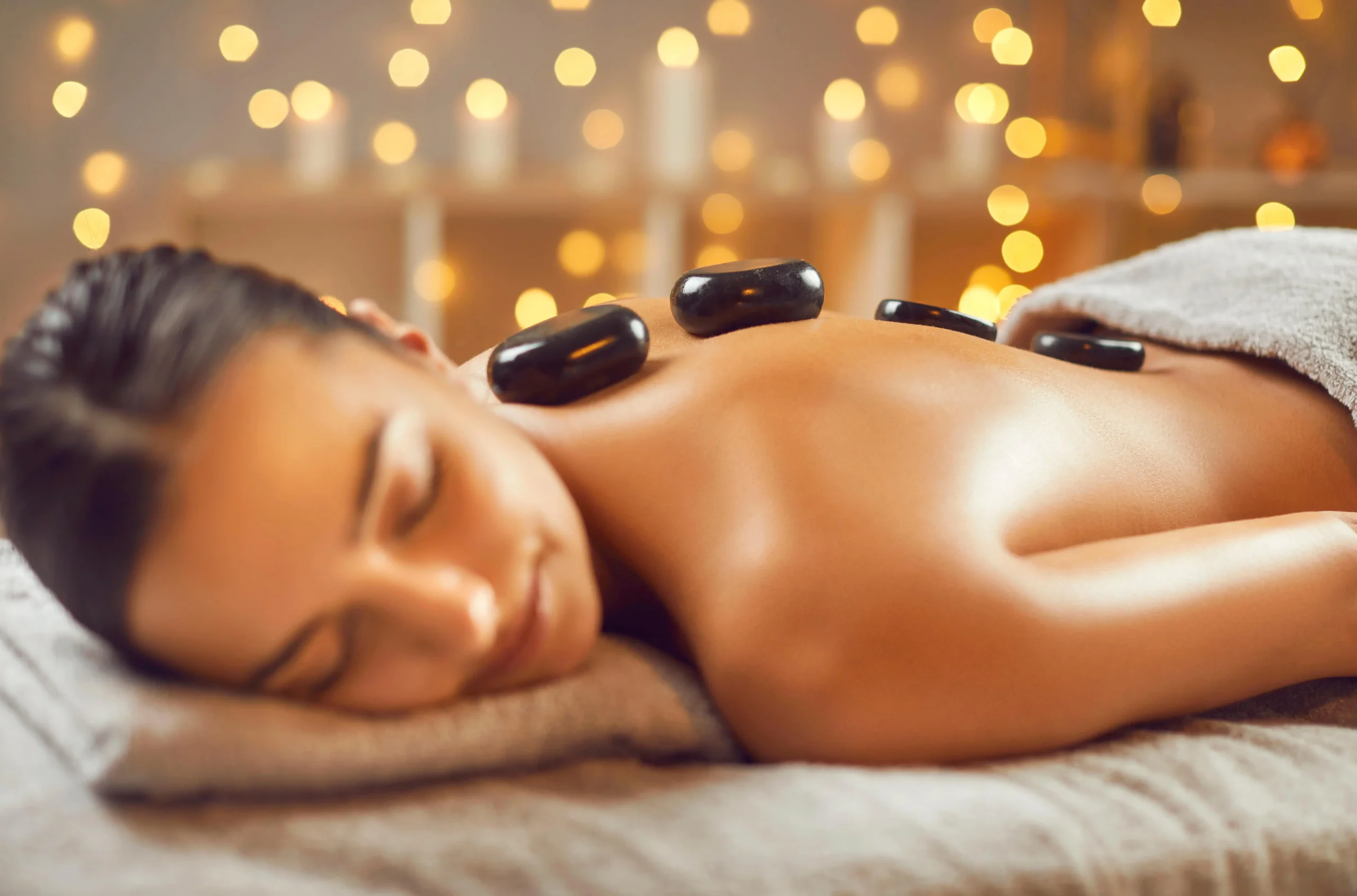 Frau liegt entspannt auf Massage Liege und Hot Stones auf dem Rücken