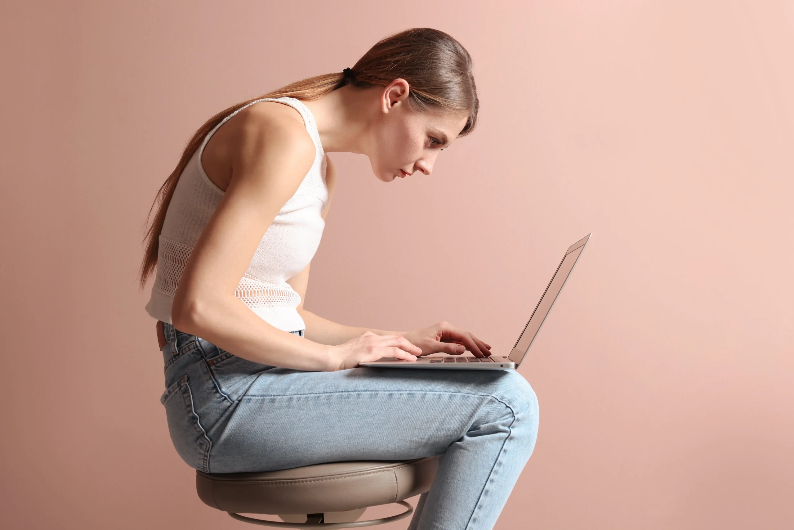 Frau sitzt auf einem Hocker am Laptop mit einer schädlichen Körperhaltung